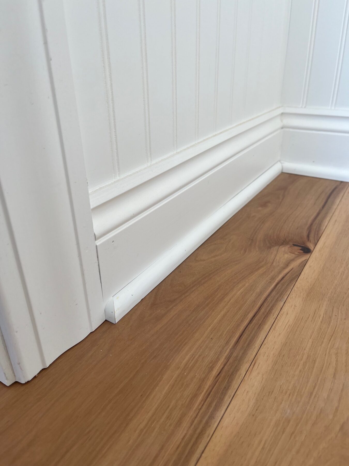 Close view of detailed white baseboard and wall trim over hardwood flooring
